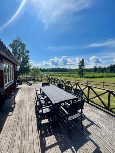 una terraza de madera con mesa de madera y bancos en Idylliskt hus med sjöutsikt., en Östhammar