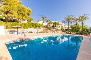 a blue swimming pool with palm trees and houses at Cap d´Or house in Moraira