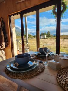 a table with plates and wine glasses and a view of a field at Cabañas Parque Chaqueihua in Hornopiren