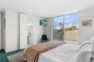 a bedroom with a bed and a large window at The Chocolate Box - Waipu Cove Holiday Home in Waipu