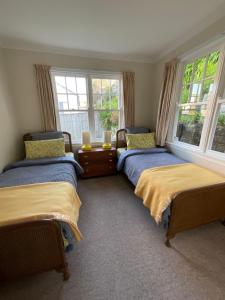 two beds in a room with two windows at Refined, Retro & Relaxing in Paraparaumu