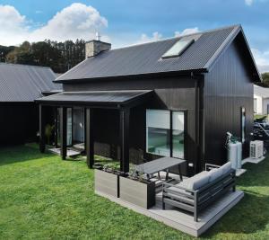 Hillbrook - a luxurious designer house في Ohauiti: منزل أسود مع مقعد على العشب