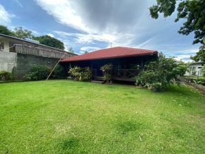 a house with a red roof and a grass yard at Chalet Mahina in Mahina