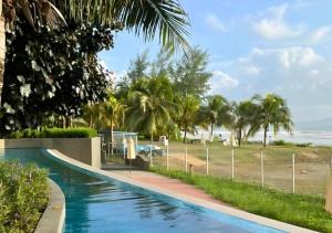 een zwembad naast een strand met palmbomen bij Timurbay Seafront Residence in Kuantan
