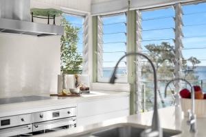 a kitchen with white counters and windows and a sink at Pacific Lodge in Hyams Beach