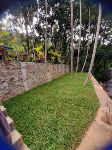 a stone wall next to a yard with trees at Artomoro Ceylon motel in Demodera