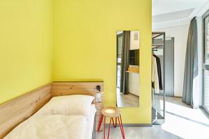 una camera da letto con pareti gialle, un letto e uno sgabello di MEININGER Hotel Köln West a Colonia