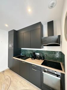 La cuisine est équipée de placards gris et d'un four avec plaques de cuisson. dans l'établissement Sacré appartement/Jardin/Parking/Wifi, à Rodez