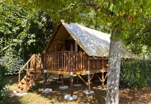 Cabaña de madera grande con techo de paja junto a un árbol en Camping Canal de Berry, en Saint-Amand-Mont-Rond