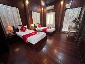 Duas camas num quarto com pisos de madeira e janelas em Villa Vieng Sa Vanh Hotel em Luang Prabang