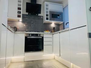 una cucina con armadi bianchi e forno nero di One bedroom posh and neat flat a Thamesmead