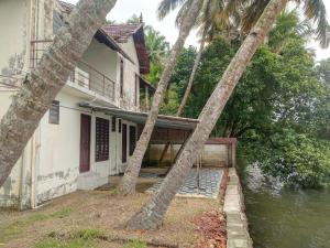 a house with two palm trees in front of a river at SANTA MARIA HOSTEL MUNROE ISLAND in Munroe Island