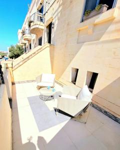 eine Terrasse mit zwei weißen Stühlen und einem Tisch in der Unterkunft Bird of Paradise in Mosta
