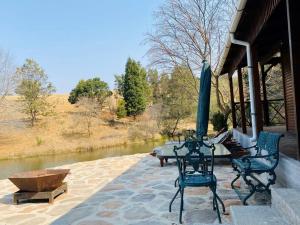 a patio with a table and chairs and a river at Brentwood Cottage in Machadodorp