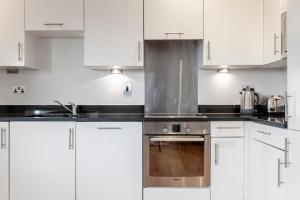 La cuisine est équipée de placards blancs et d'un four avec plaques de cuisson. dans l'établissement Beautiful 1BDR Apartment near Clapham Common, à Londres