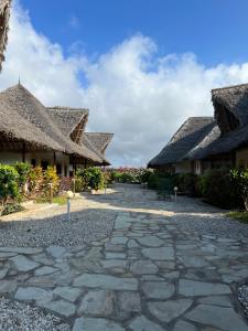 a stone walkway between two buildings with thatched roofs at BeB Sardegna2 Anjumasa village in Watamu