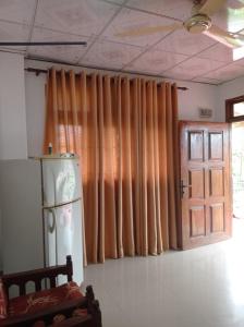 Habitación con cortinas de color naranja, nevera y puerta. en Weligama Elite Guest, en Weligama