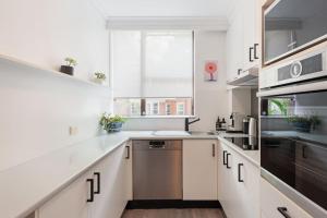 a kitchen with white cabinets and a stainless steel dishwasher at Harbourside Style, 2 Bed, A/C, Pool -Elizabeth Bay in Sydney