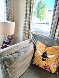 a couch with a pillow with a bee on it at Eden Breaks, Mallard Lake in Cirencester