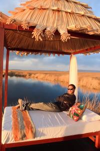 a man laying on a bed under a thatch roof at Titicaca Ecolodge Perú in Puno