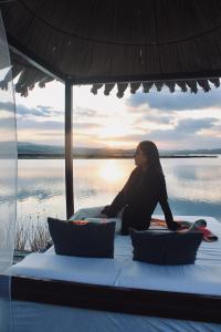 a woman sitting on a bed in front of the water at Titicaca Ecolodge Perú in Puno