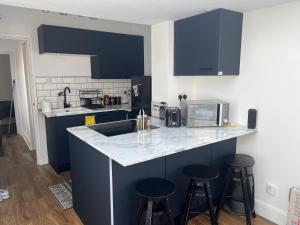 Newly refurbished 1-Bed Apartment in Croydon SE25 في لندن: مطبخ مع دواليب زرقاء وكاونتر مع الكراسي