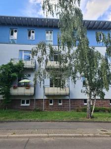 a blue building with white balconies and a tree at Casa Frida - Business flat near BER, kitchen, bathroom, balcony, workspace, 24" Monitor, Wifi, SmartTV, Netflix, car park in Berlin