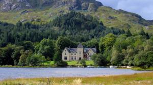 a house on the shore of a lake with a mountain at Glenfinnan House Hotel in Glenfinnan