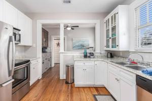 uma cozinha branca com armários brancos e pisos em madeira em Festive Nest - Tranquil Escape Close to the Beach em Galveston