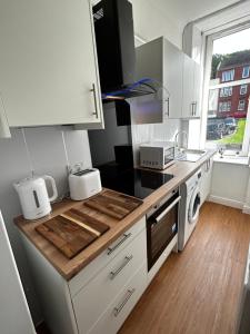 a kitchen with white cabinets and a wooden counter top at THE LAZY LION - Spacious 2 Bedroom - Town Centre Holiday Home Apartment in Port Glasgow