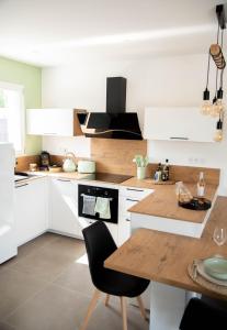 une cuisine avec des placards blancs et une table en bois dans l'établissement Les Brézines - Maison Clim Terrasse Plancha au coeur de Mus 3 Etoiles - MaisoncarréeConciergerie, à Mus