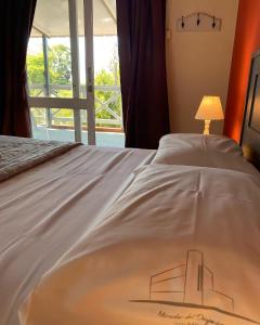 a bed with a white bedspread with a lamp and a window at Hotel Mirador del Dayman in Termas del Daymán