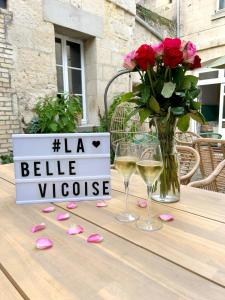 stół z dwoma kieliszkami wina i wazonem róż w obiekcie La Belle Vicoise w mieście Vic-sur-Aisne