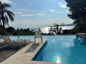 a swimming pool with two chairs and the ocean at BELÍSSIMA CASA ILHABELA in Ilhabela