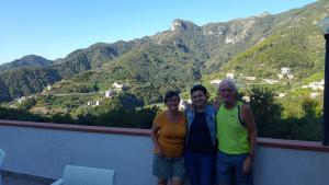 3 persone in piedi su un balcone con montagne sullo sfondo di Hotel affittacamere novella a Tramonti