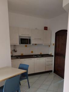 una cucina con armadi bianchi, tavolo e sedie blu di Appartamento Calarossa Sardegna CasaRosa a Isola Rossa
