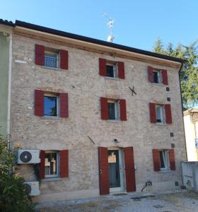 ein großes Steingebäude mit roten Fensterläden in der Unterkunft CASA TOFFOLI SOLIGO - locazioni turistiche in Soligo