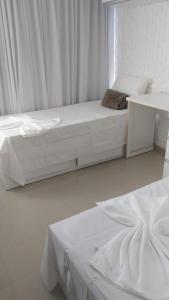 a white bedroom with two beds and a table at Villa dos Diamantes - 16 in Porto Seguro