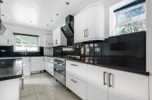 una cocina con armarios blancos y encimeras negras en HARTFORDE HOUSE, en Borehamwood