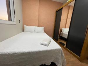 um pequeno quarto com uma cama branca e um espelho em Bexp Spaces | Mackenzie Alphaville em Aldeia