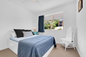 a white bedroom with a bed and a chair at Surf Dance Apartments in Coolum Beach