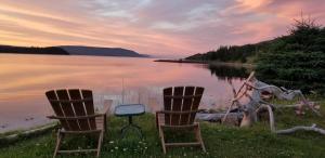 due sedie sedute accanto a un corpo d'acqua di St Ann's Motel & Cottage a Baddeck