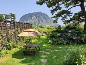 a picnic table with an umbrella in the grass at Wind Jeju Cafe & Pension in Seogwipo