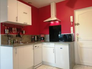 a kitchen with white cabinets and a red wall at Nuit étoilée in Béthune