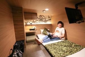 a woman sitting on a bed with a laptop at HOTEL Cargo Shinsaibashi in Osaka
