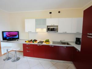 Il comprend une cuisine équipée de placards rouges, d'un évier et d'une télévision. dans l'établissement Residence Eden Apartments, à Argegno