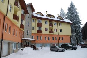 un grand bâtiment avec des voitures garées dans la neige dans l'établissement PM Services Royal Plaza Apartments, à Borovets