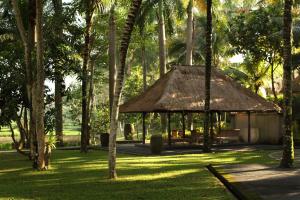 uma cabana com telhado de palha num parque com palmeiras em The Ubud Village Resort & Spa em Ubud