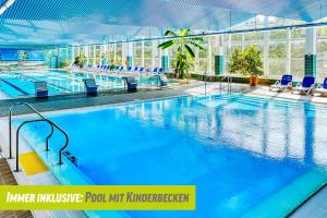 une grande piscine avec des chaises bleues dans un bâtiment dans l'établissement AHORN Berghotel Friedrichroda, à Friedrichroda