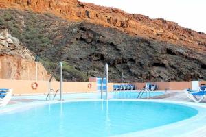 a large swimming pool with chairs and a mountain at Apartamento con diseño moderno y piscina Taurito in Taurito